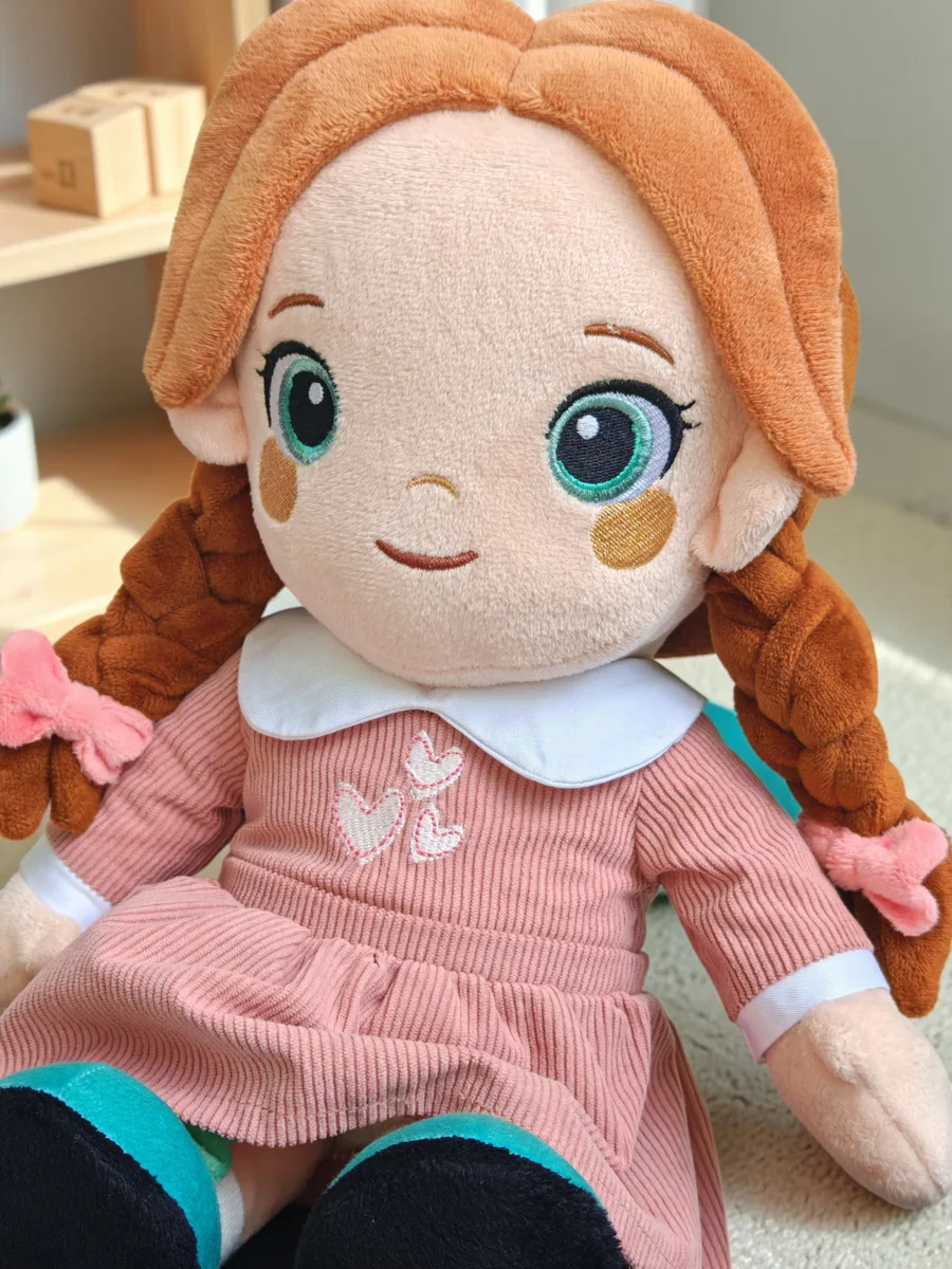 Playnitive Lotti, eine Plüschpuppe mit geflochtenen roten Haaren, einem altrosa Cordkleid und petrolfarbenen Schuhen.